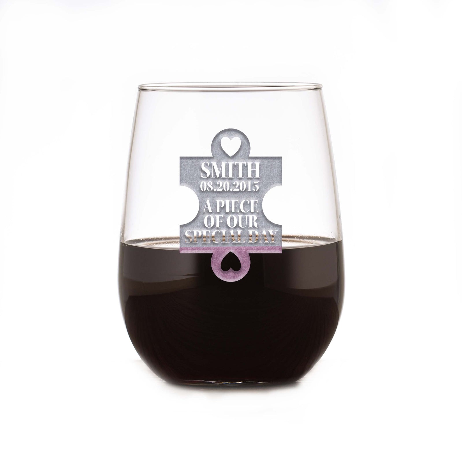 Stemless wine glass filled with dark wine, deep-etched with a puzzle-piece design reading "Smith, 08.20.2015, A Piece of Our Special Day," on a white background.