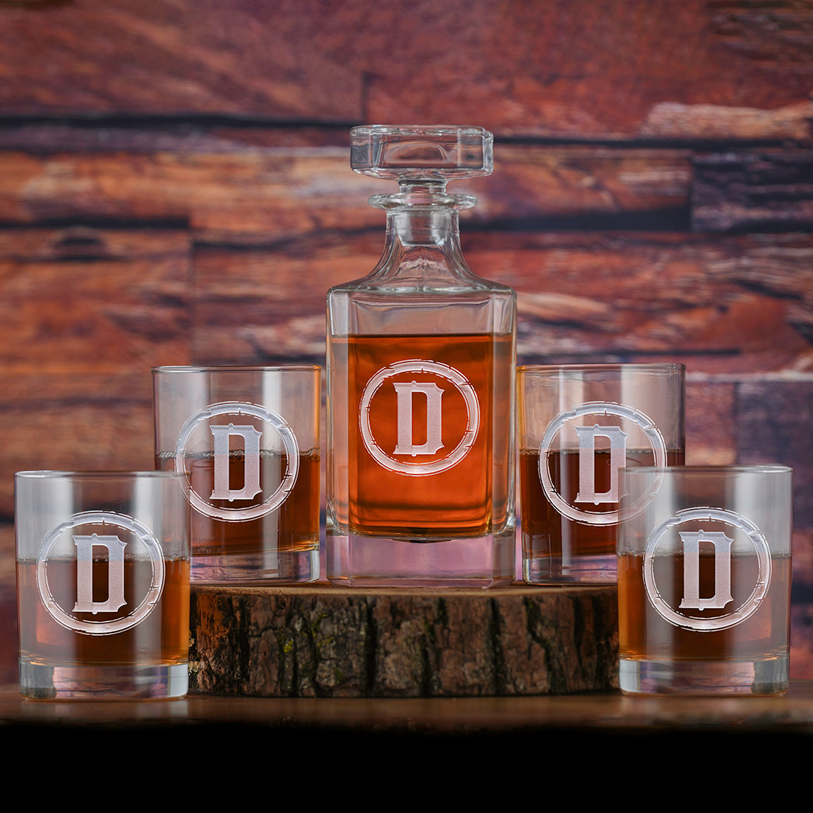 Square whiskey decanter and four matching rocks glasses, each deep-carved with a block-letter initial inside a barbed circle, filled with amber spirit.