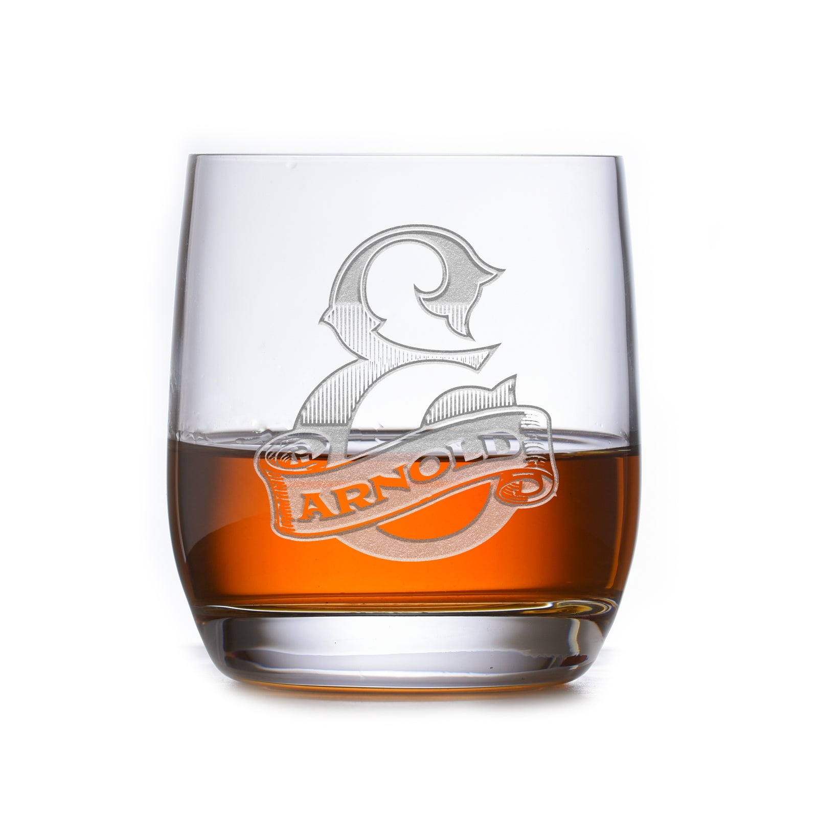 Clear rocks glass filled with amber liquid, deep-carved with a shield reading "E, Arnold," on a book background.