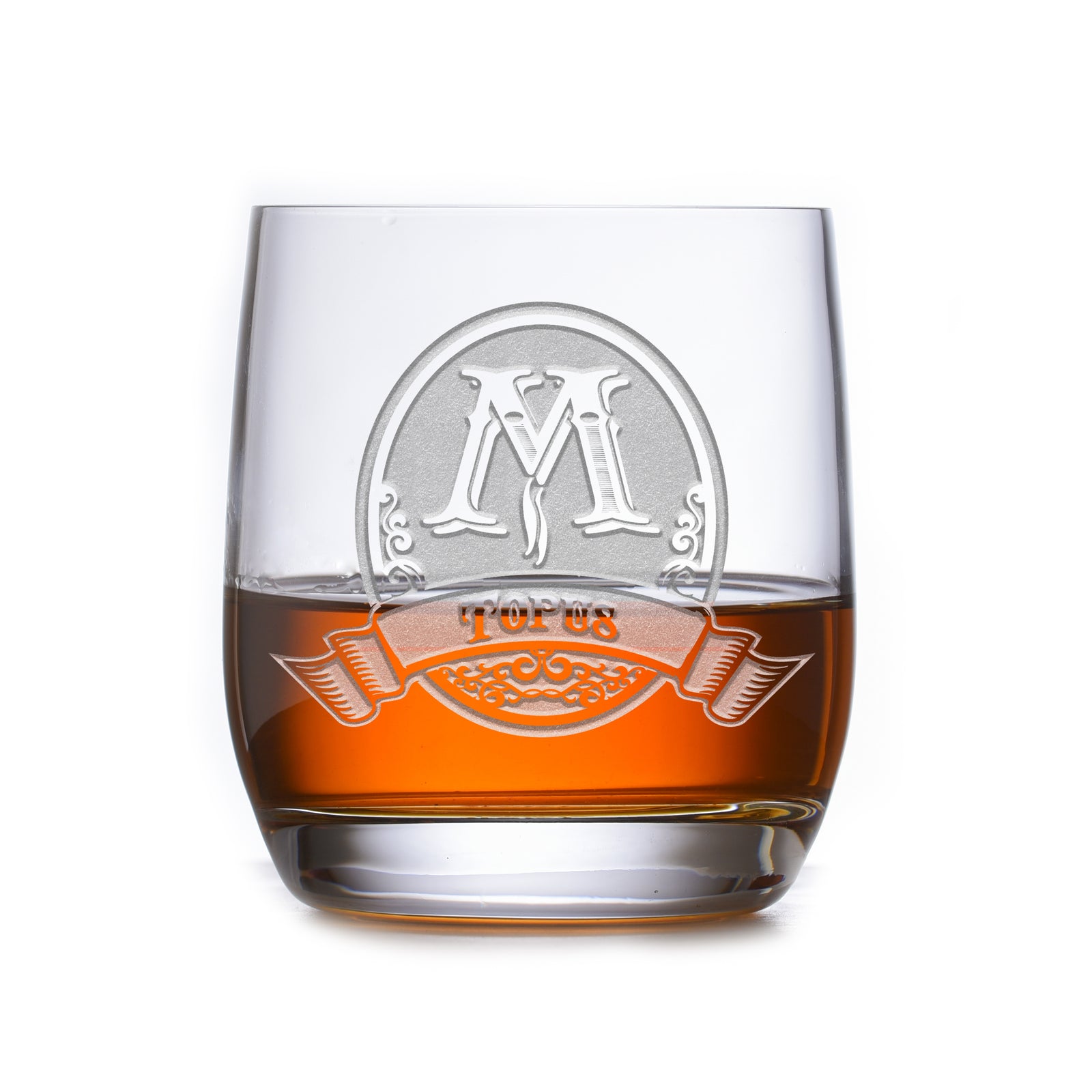 Rocks glass filled with amber liquid, deep-carved with an oval crest reading "M, Topus," on a white background.