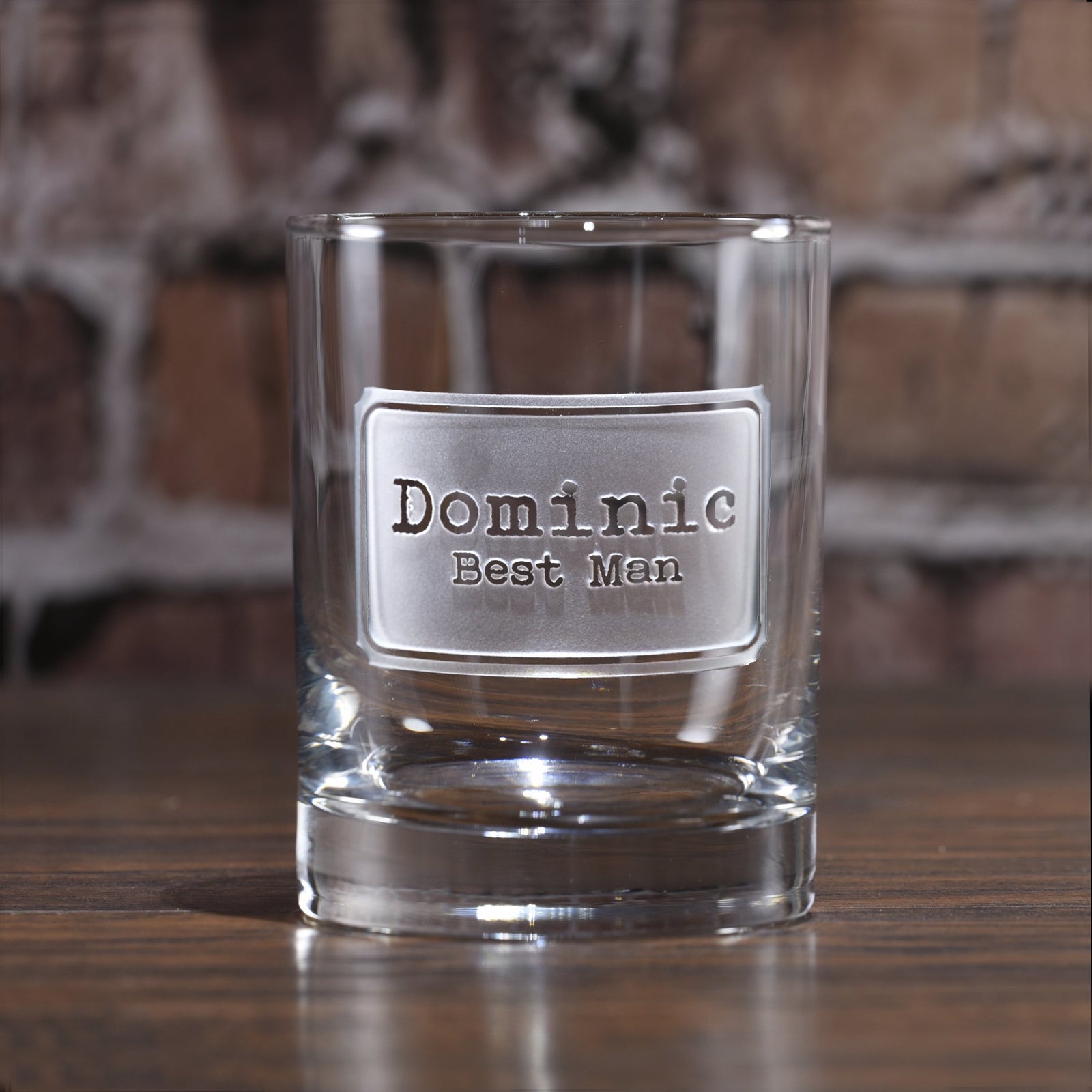 Rocks glass deep-carved with a badge reading "Dominic, Best Man," on a brick background.