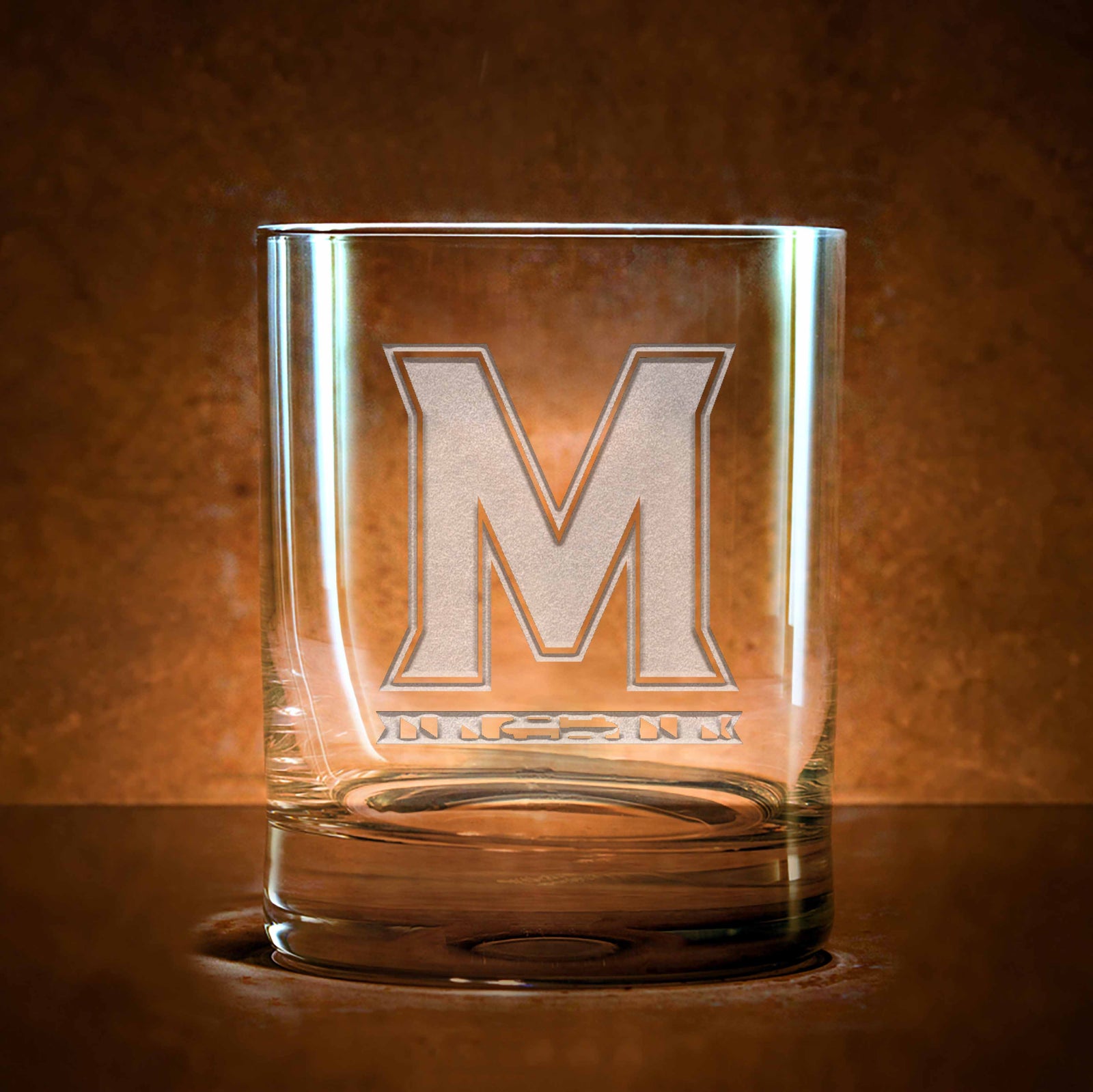 Rocks glass deep-carved with the Maryland Terrapins "M" logo, on a dark background.